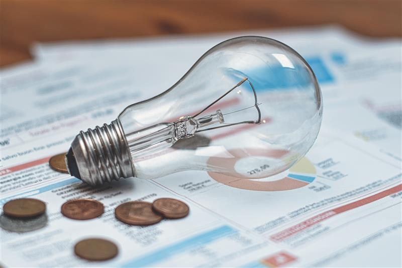 Mesa de escritório com várias contas de luz, moedas e uma lâmpada